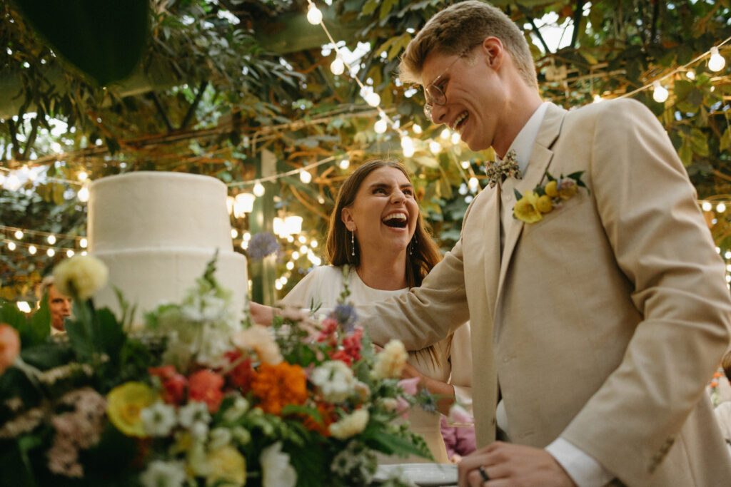 bride and groom laugh while cutting their cake