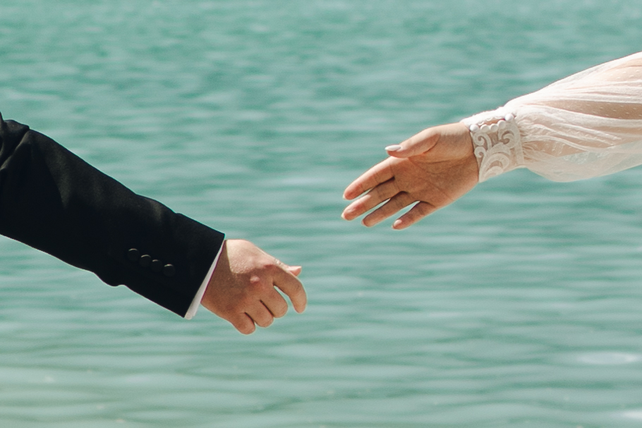 bride and groom reach to hold hands at lake louise