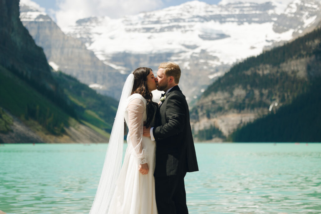 bride and groom kiss at blue lake, lake louise